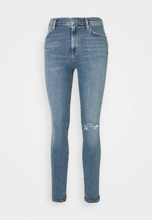 Jean skinny bleu clair à taille haute, avec bouton et fermeture éclair à l'avant, passants de ceinture et une petite déchirure sur le genou droit.