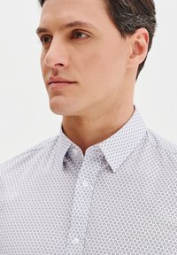 Biała koszula z kołnierzykiem zapinanym na guziki, z małym, okrągłym wzorem w granatowym kolorze. Slim fit, o gładkiej teksturze i klasycznym designie.