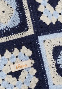 Coperta all'uncinetto con quadrati blu navy, azzurro chiaro e crema, con motivi floreali e geometrici, con etichetta in tessuto "Blkvis" cucita sopra.