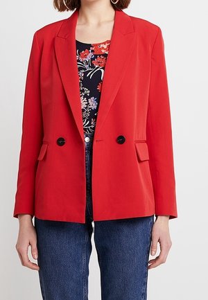 Blazer rouge avec un design structuré, fermeture à double bouton, revers, et boutons noirs, associé à un haut à imprimé floral.