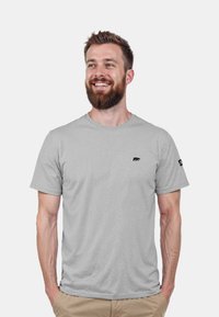 Hellgraues T-Shirt aus einem weichen Stoff, mit einem kleinen schwarzen Bärenlogo auf der Brust und einem Etikett am Ärmel. Kurze Ärmel und Rundhalsausschnitt.