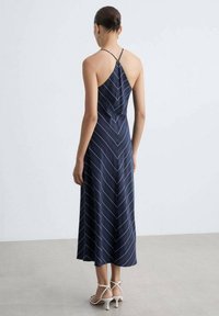 Tmavě modré šaty s lehkou, hladkou texturou. Mají bezrámový design a tenké ramínka, se bílými diagonálními pruhy vytvářejícími chevronový vzor.