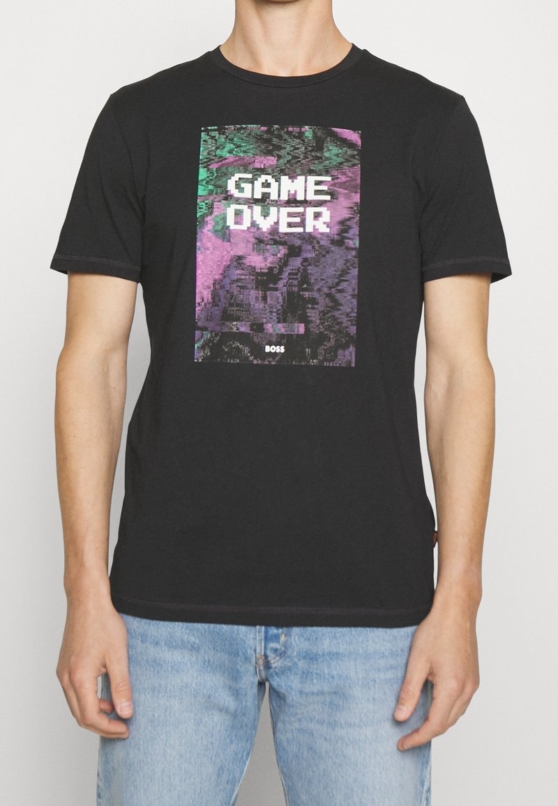 T-shirt noir à manches courtes avec un graphisme pixélisé "GAME OVER" en blanc et violet, doté d'une texture en coton lisse.