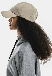 Cappellino beige realizzato in tessuto leggero, con visiera curva e cinturino regolabile; abbinato a una felpa grigia con cappuccio.