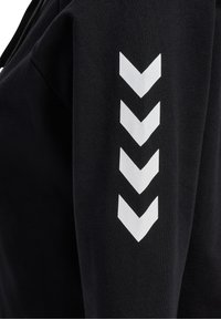 Tissu noir à texture lisse avec des rayures chevron blanches le long de la manche. Le design met l'accent sur la simplicité et le contraste.