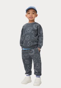 Graues Set aus Sweatshirt und Hose mit weißen Cartoon-Mustern, ergänzt durch einen blauen Akzent am Kragen und an den Bündchen sowie weißen Turnschuhen.