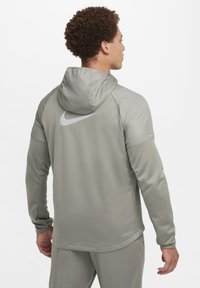 Sudadera gris de Nike con un diseño texturizado, capucha ajustable y logo reflectante. Las mangas largas y el corte entallado mejoran la funcionalidad de la ropa deportiva.
