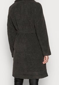 Cappotto in pile marrone scuro con vita aderente, maniche lunghe e colletto a scialle, caratterizzato da una superficie morbida e testurizzata e un design di lunghezza media.