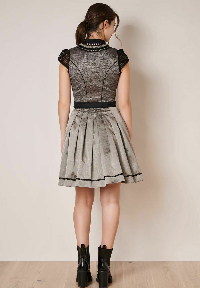 Graues Kleid mit strukturiertem Oberteil, kurzen Ärmeln und plissiertem Rock. Schwarze Akzente an Taille und Saum. Modell trägt schwarze Knöchelstiefel.