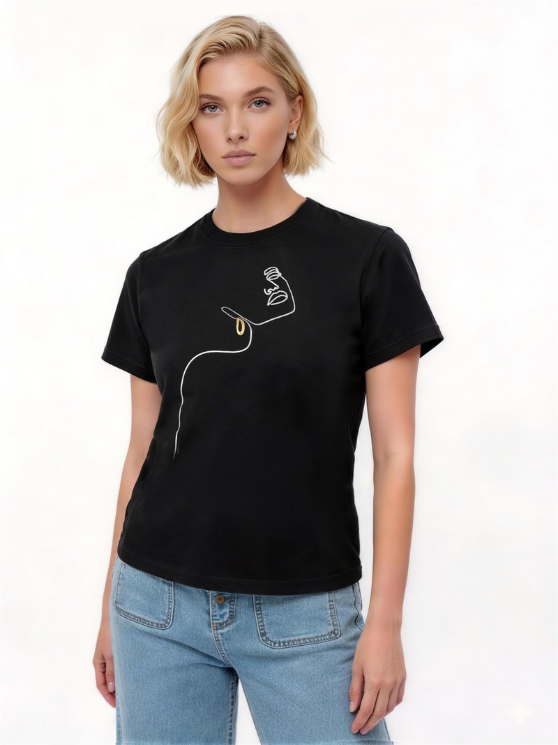 Blonde vrouw die een zwart t-shirt draagt met een minimalistische witte lijntekening van een gezicht met een gouden oorbel, gecombineerd met lichtblauwe spijkerbroek.