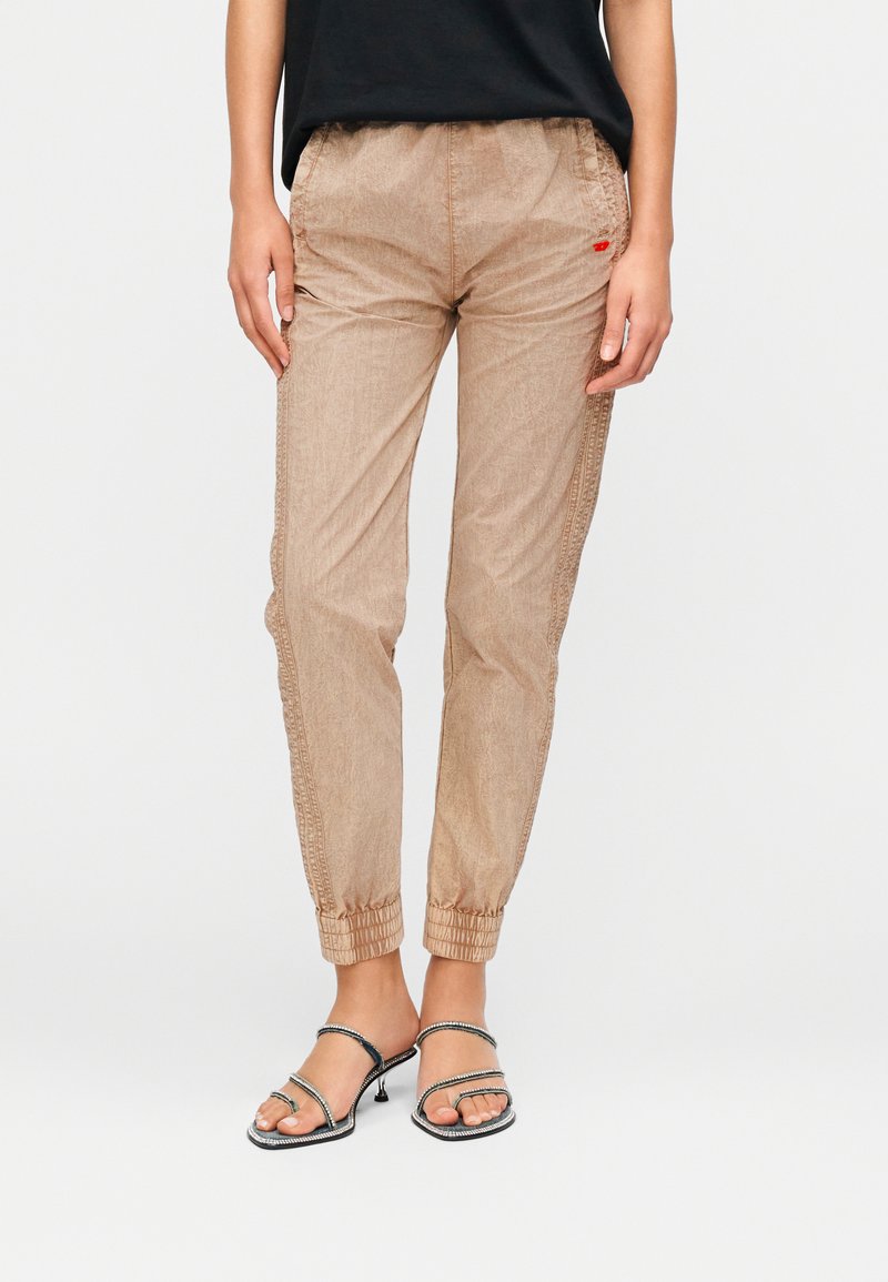 Μπεζ παντελόνια με κορδόνι στη μέση, ελαστικές μανσέτες, διακριτικό υφή ύφασμα και λεπτομέρειες στα πλευρικά ραφές. Φοριούνται με μαύρα σανδάλια με λουράκια και τακούνι.