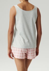 Szary bawełniany top na ramiączkach z okrągłym dekoltem w zestawieniu z różowymi szortami w kratkę o miękkiej fakturze i jasnych, pastelowych kolorach.