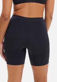 Pantalones cortos negros sin costuras con una textura suave, de largo hasta el muslo y con una cinturilla alta. Presentan un centro reforzado para mayor comodidad.
