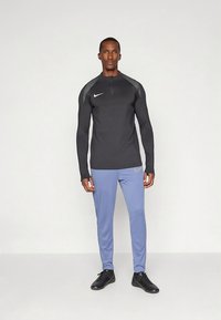 Black long-sleeve top with grey accents and a half-zip, paired with light blue athletic pants featuring a small logo. Worn with black sneakers.