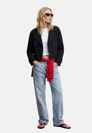 Woman wearing black cropped jacket, white cropped shirt, light blue jeans, red sweater tied around waist, red flip-flops, and black sunglasses.