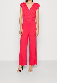 Fuchsia jumpsuit with short sleeves, deep V-neck, and wide legs. Made from a soft fabric, featuring subtle draping along the bodice.