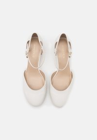 Valkoiset slingback-kengät, joissa on sileä, matta pinta; pyöreä kärki; säädettävä hihna kultasävyisellä varusteella; vaaleanbeige sisäpohja.