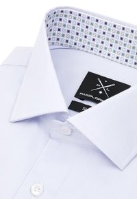 Jasnoniebieska koszula zapinana na guziki z wzorzystym wewnętrznym kołnierzykiem w odcieniach fioletu i zieleni. Posiada czarną metkę z nazwą marki i rozmiarem.