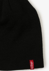 Musthave musträni müts, millel on soonikstruktuur, punase Levi's logo sildiga küljel. Pehme materjal, tihedalt sobiv disain.