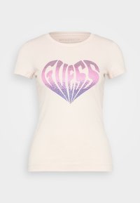 Camiseta de algodón de manga corta en un rosa claro, con un diseño en forma de corazón que lleva la palabra "GUESS" en strass de colores púrpura y rosa en degradé.