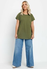 Oliven grøn bomulds T-shirt med korte ærmer, parret med brede lyse blå denimjeans og beige fodtøj. Enkel, afslappet design.