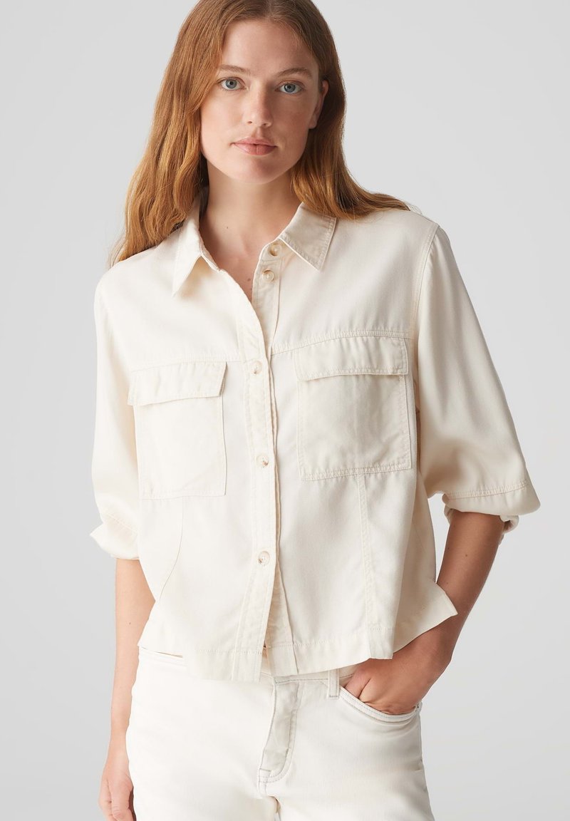 Camicia beige a maniche corte con colletto, due tasche sul petto e una vestibilità rilassata. Realizzata in tessuto morbido e leggero.