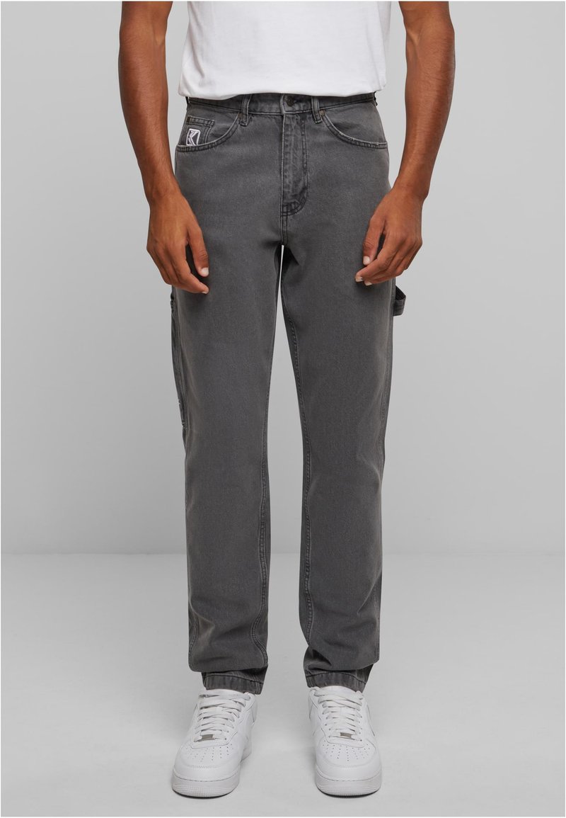 Šedé džíny cargo s bočními kapsami, standardní střih, zúžené nohavice a jemně vybledlá textura, spárované s bílými teniskami.