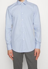 Lichtblauw overhemd met knopen, lange mouwen, subtiele glans en een afgeronde zoom. Heeft witte knopen en een klassiek kraagontwerp.