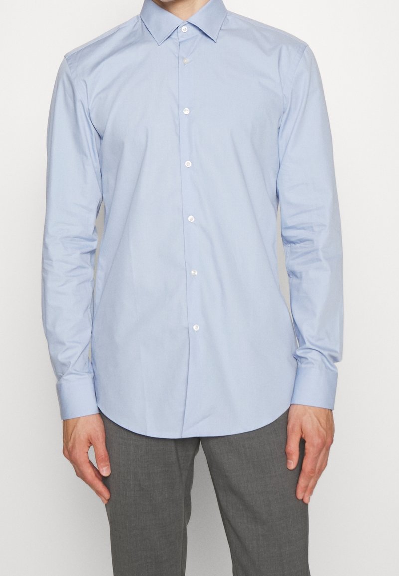 Lichtblauw overhemd met knopen, lange mouwen, subtiele glans en een afgeronde zoom. Heeft witte knopen en een klassiek kraagontwerp.