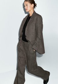 Blazer grigio in lana e pantaloni a gamba larga abbinati, con una vestibilità rilassata, rever appuntiti e una finitura texture. Top nero sotto.