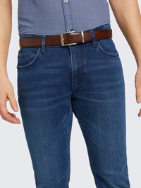 Jeans en denim bleu foncé avec une coupe slim, présentant des décolorations légères. Assortis à une ceinture en cuir marron avec une boucle en argent.