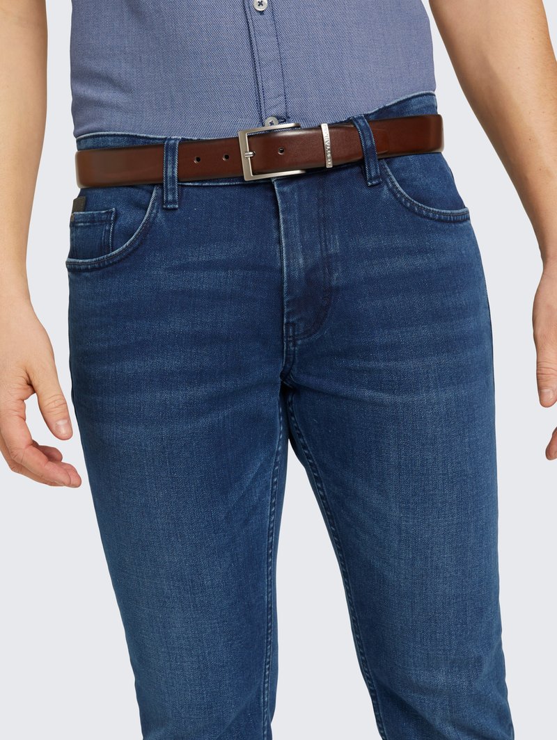 Jeans en denim bleu foncé avec une coupe slim, présentant des décolorations légères. Assortis à une ceinture en cuir marron avec une boucle en argent.