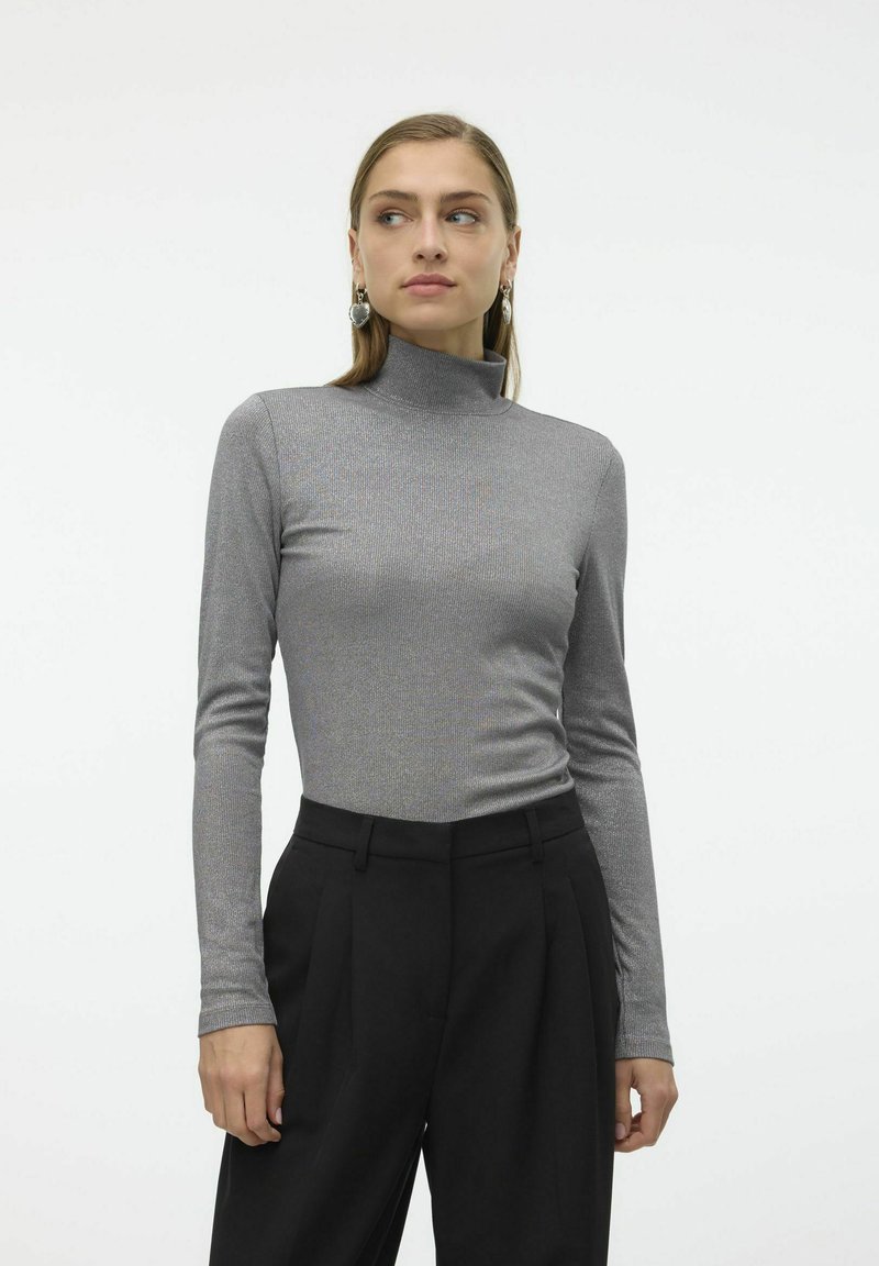 Haut à col roulé gris à manches longues, texture côtelée, design ajusté. Porté avec un pantalon noir taille haute.