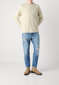 Ljust beige crewneck sweatshirt med en texturerad finish, i kombination med blå slitna jeans och tanfärgade ankle boots med gummisula.
