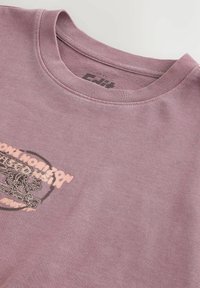 Hellviolettes T-Shirt mit rundem Ausschnitt, geripptem Kragen und verblasstem Löwengrafik- und Textdruck auf der Brust, flach auf weißem Hintergrund liegend.