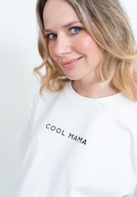 Bílý krátký rukáv tričko s potiskem "COOL MAMA" v černé barvě. Měkká tkanina, uvolněný střih a kulatý výstřih. Minimalistický design.
