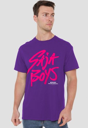 Purple cotton t-shirt featuring bold pink text "SAJA BOYS" and a smaller brand logo. Short sleeves and a round neckline.