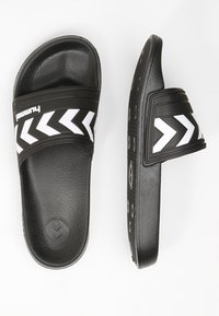 Svarta slidesandaler med en texturerad sula, med ett brett horisontellt rem med vita chevron-mönster. Gummimaterial, enkel design.