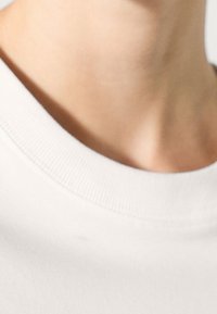 White cotton t-shirt with a crew neckline, featuring ribbed trim. The fabric appears soft with a smooth texture and slight sheen.