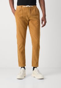 Tanen corduroy broek met een trekkoord in de taille, plooien aan de voorkant, taps toelopende benen en ribbelstructuur, gecombineerd met witte sneakers.