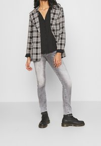 Blazer a cuadros en blanco y negro con dos bolsillos, combinado con una blusa negra de botones y jeans ajustados grises. Botines negros con cordones.