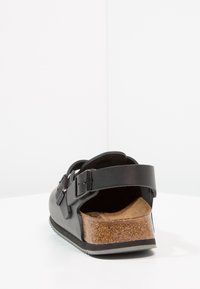 Black sandal with adjustable straps, a cork footbed, and textured rubber sole. Features an open back and a smooth upper material.