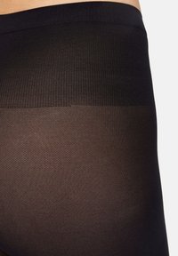 Sorte strømpebukser med et tekstureret strikket mønster øverst, der glider over i en gennemsigtig finish. Livremmen er bred og elastisk.