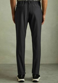 Pantaloni sport negru cu o textură netedă, talie elastică și două bă pockets; purtați cu adidași negri și detalii ușoare la gleznă.