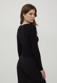 Czarny dopasowany sweter z długim rękawem i okrągłym dekoltem, w połączeniu z czarną spódnicą. Srebrne wyraziste kolczyki wiszą z uszu modelki.