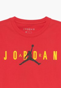 Červené bavlněné tričko s velkým černým siluetou skákající postavy a žlutým nápisem "J O R D A N." Klasický kulatý výstřih.