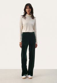 Maglione a collo alto crema abbinato a pantaloni larghi in velluto verde. Tessuto morbido, vestibilità rilassata e design minimalista. Sneakers bianche con suole chiare.