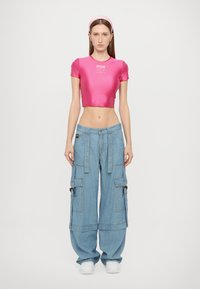 Prigludusi rožinė satino mini palaidinė su trumpomis rankovėmis, derinama su laisvomis mėlynomis džinsinėmis cargo kelnėmis, turinčiomis dekoratyvių detalių ir didelių kišenių.