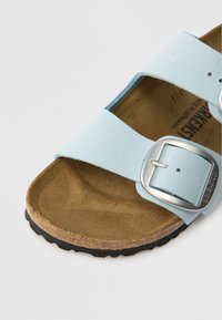 Ανάλαφρη μπλε σαγιονάρα με δύο φαρδιές λωρίδες, ασημένια μεταλλική αγκράφα και υφασμάτινη καφέ φελλώδη σόλα. Μαύρη ελαστική σόλα.