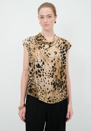 Krátký rukáv halenka v béžové barvě s leopardím vzorem. Měkká, splývavá tkanina s kašmírovým výstřihem a uvolněným střihem. Černé kalhoty nosené pod tím.